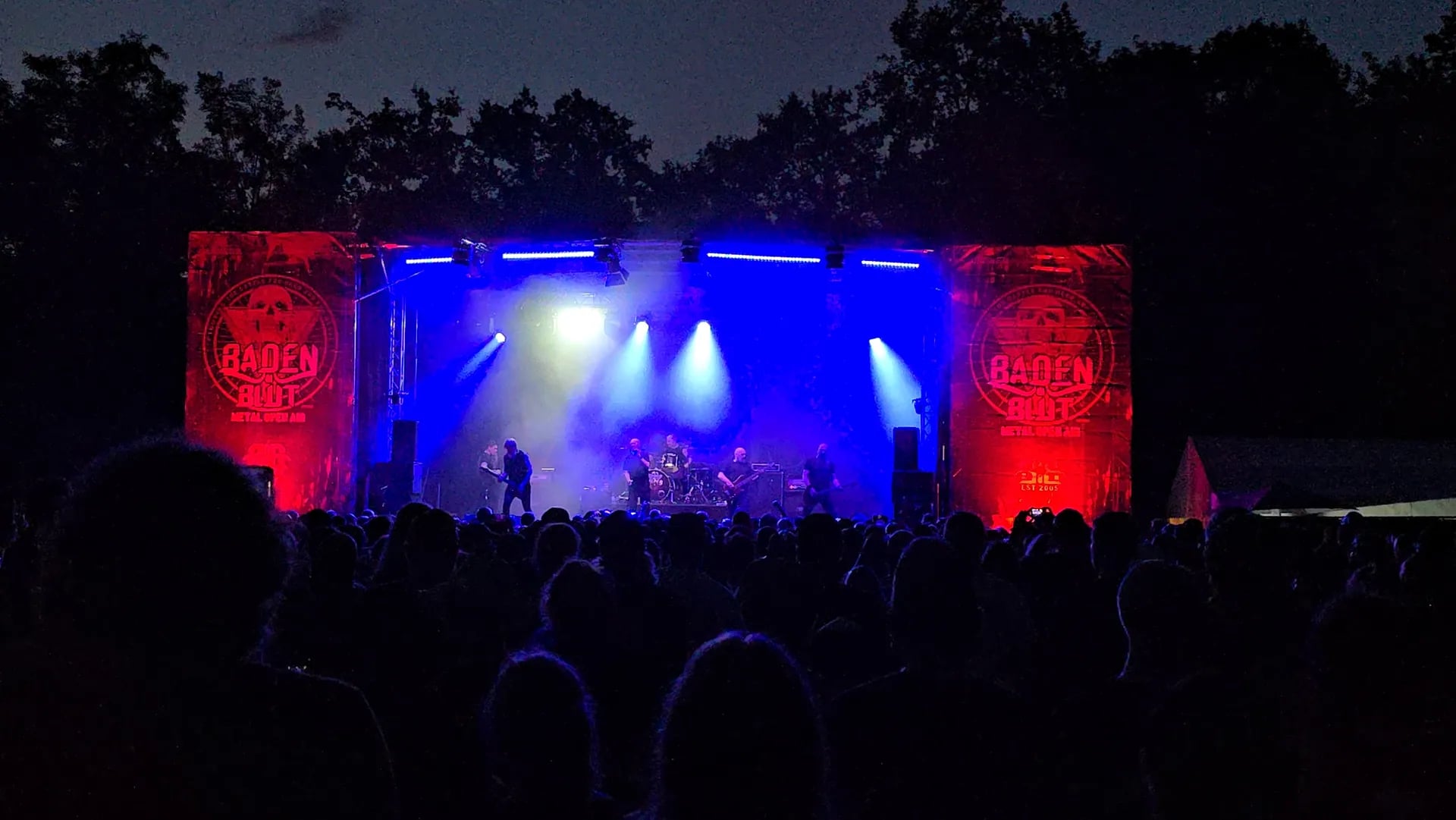 Bühne bei Nacht in blauem und rotem Licht, Band im Gegenlicht vor dem Publikum